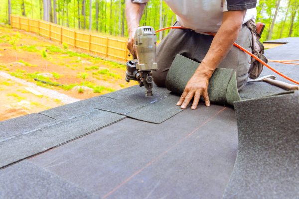 Construction worker by roofer installing new bitumen shingles on roof used air pneumatic nail gun