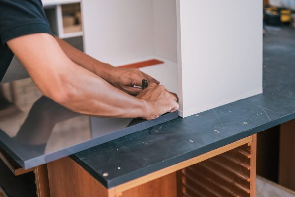 Hands of a man fixing a hinge on a surface for a kitchen that are building in a workshop