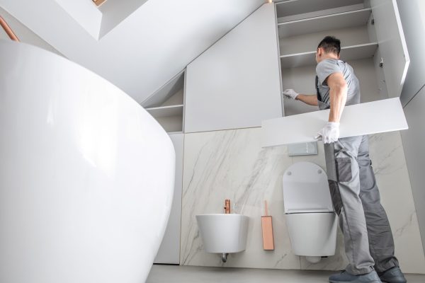 New Bathroom Interior Finishing. Caucasian Men in His 30s Assembling Modern Cabinets. Home Interior Remodeling Theme.